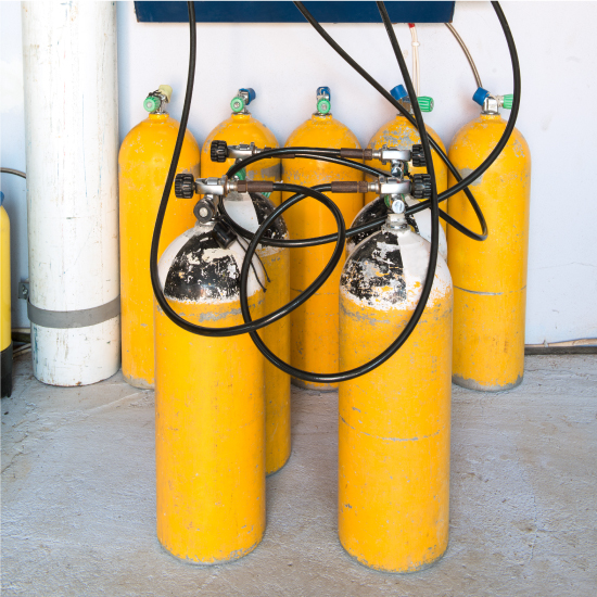 Yellow scuba tanks getting filled with air. One row of 5 scuba tanks in the background.