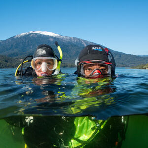 Photo of two scuba divers in water with heads above water in a lake with mountains in the background. Depicting altitude diving.